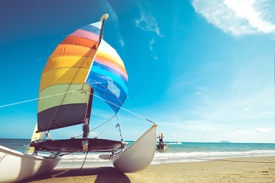 סירת מפרש צבעונית על חוף טרופי בקיץ.