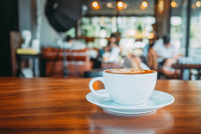 Vit kopp varmt kaffe på bordet i café med folk